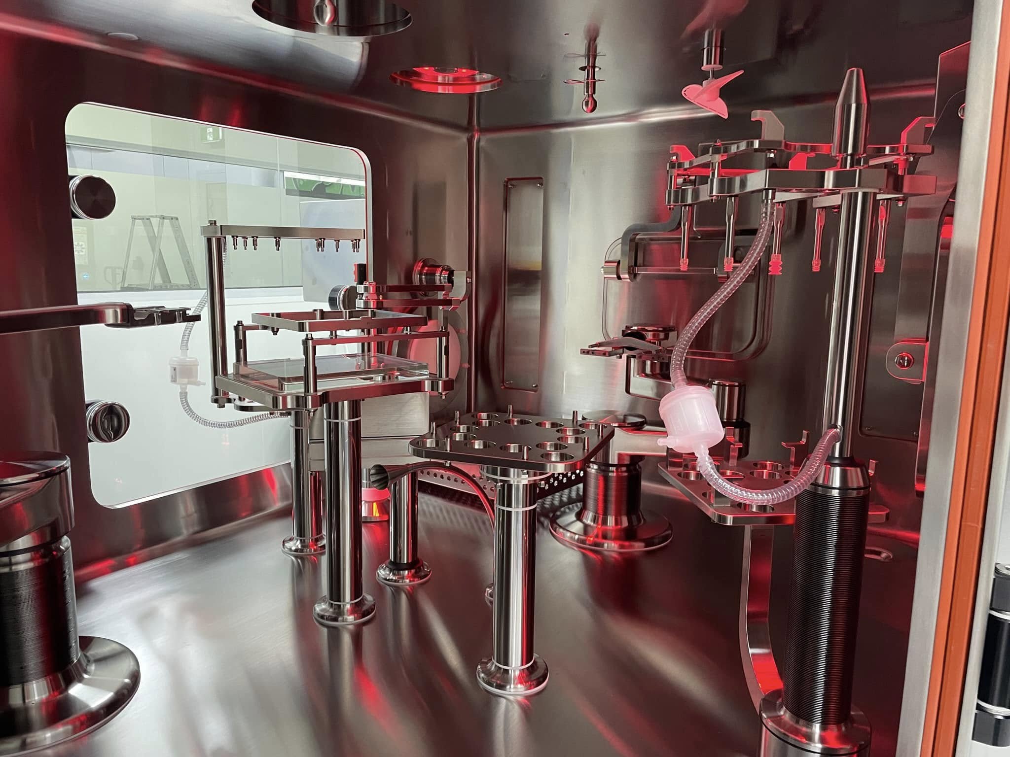 Stainless process vessel and isolator under red light in a pharmaceutical facility.