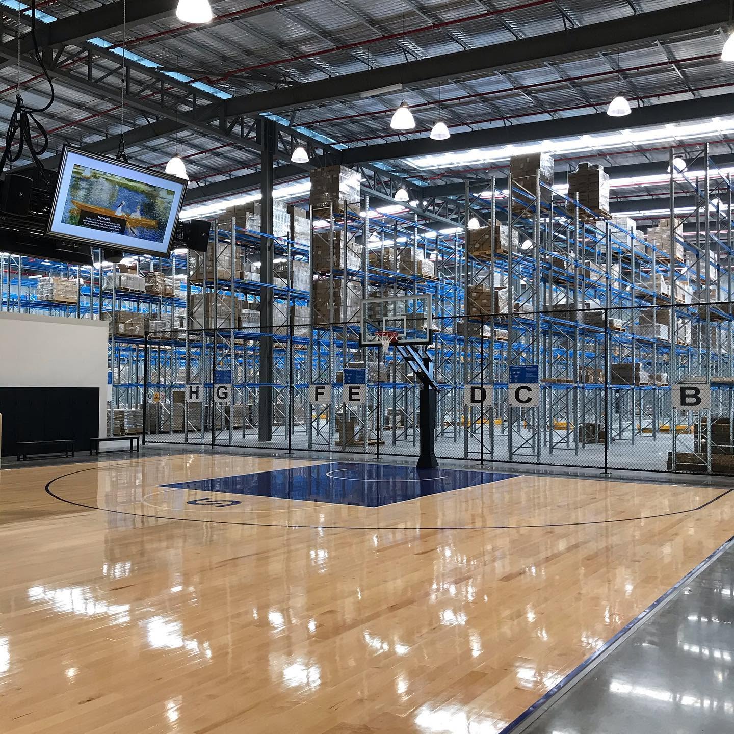 Warehouse with a basketball court set among high-bay racking.